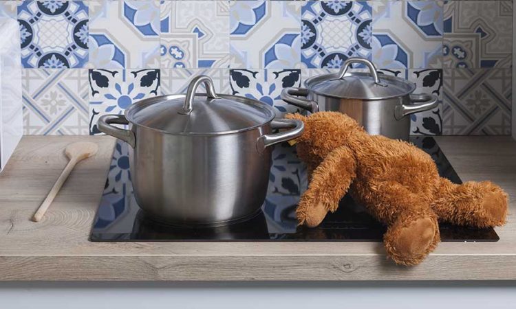 Teddy liegt auf Herd zwischen Töpfen.