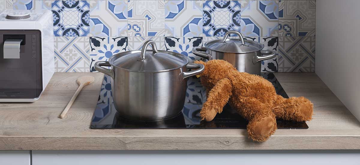 Teddy liegt auf Herd zwischen Töpfen.