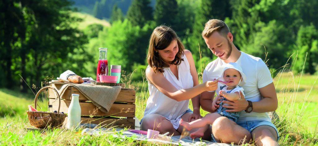 Familie mit Kind sitzt in der Natur und macht ein Picknick mit dem Growing Geschirr aus nachhaltigen Materialien