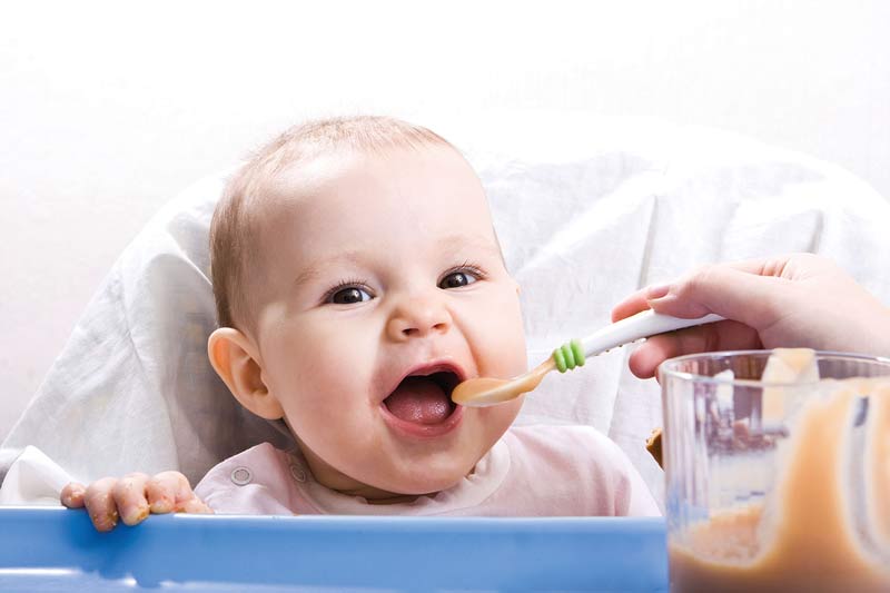 Baby bekommt Brei gefüttert, nachdem es mit dem Essen gespielt hat