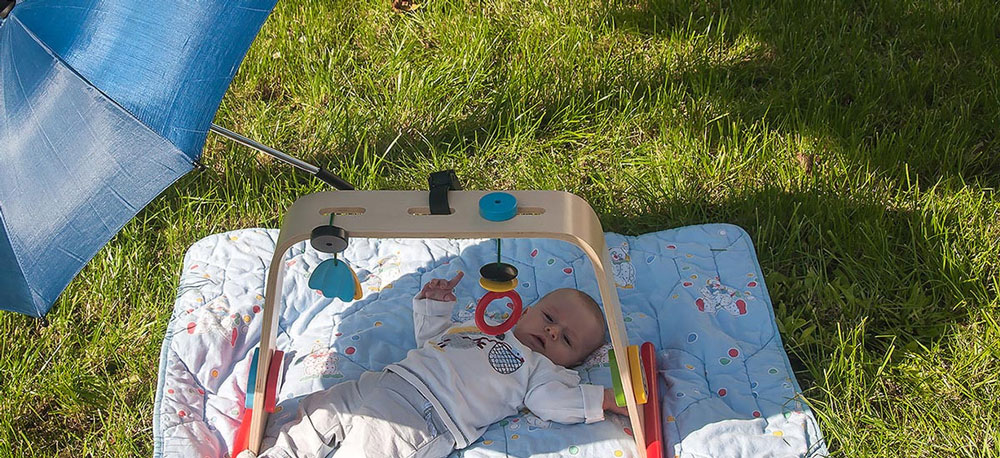 Kind liegt auf einer Decke im Freien, neben ihm liegt ein Sonnenschirm um es zu bedecken