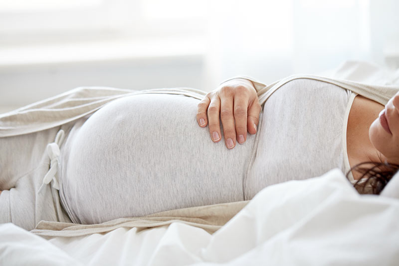 Schwangere Frau liegt auf dem Rücken, sie zeigt Übelkeits-Beschwerden