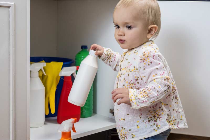 Kind hat Reinigungsmittel in der Hand und steht vor dem Putzschrank