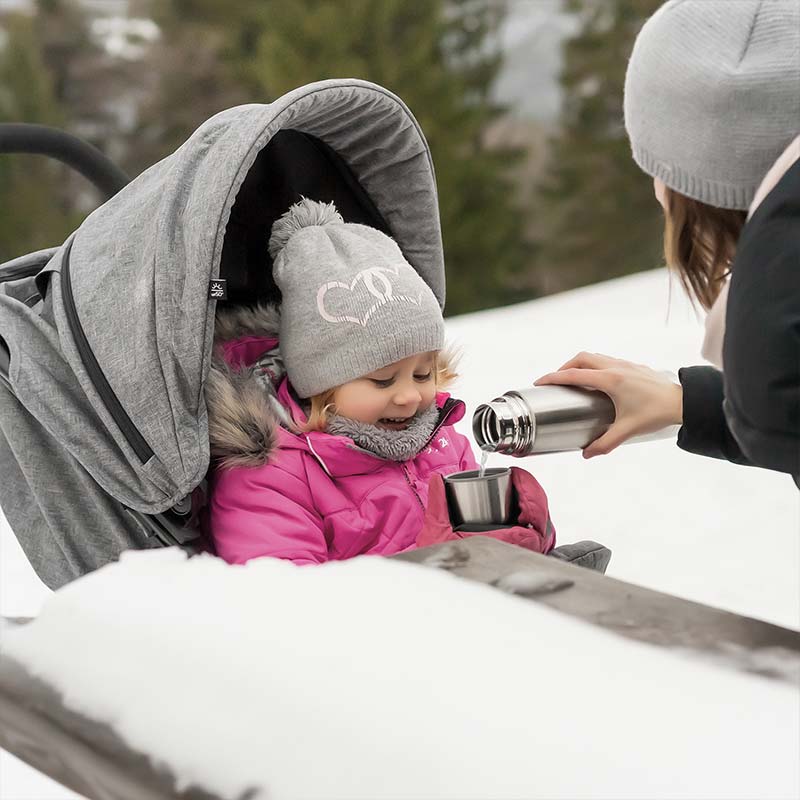 Mutter gibt dem Kind im Kinderwagen etwas zu trinken mit der Isolierflasche