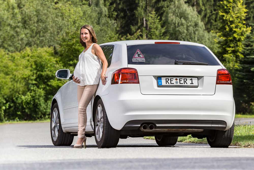 Schwangere Frau lehnt sich an das Auto an