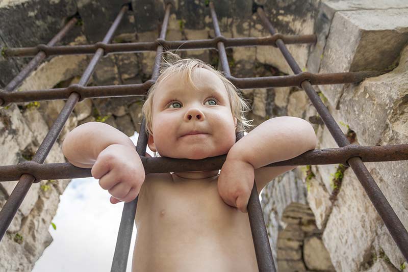 Kind hinter Gitterstäben, steckt den Kopf durch