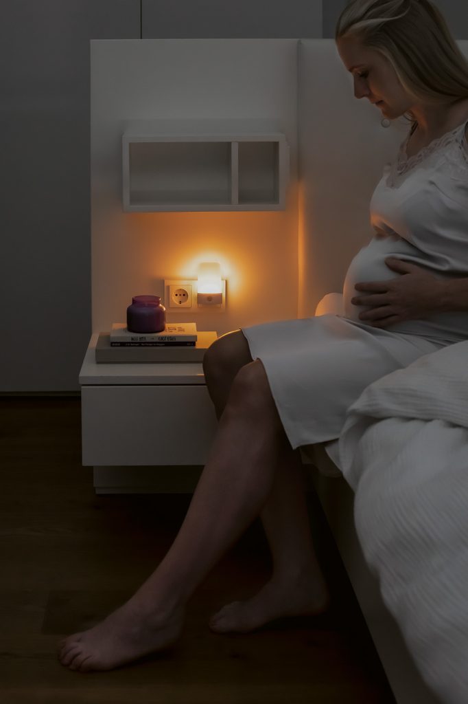 Schwangere sitzt auf Bett mit Nachtlicht in der Steckdose